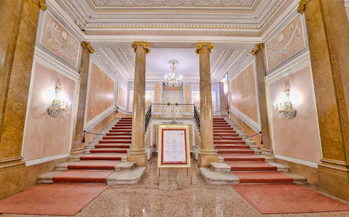 Grand staircase inside La Fenice Opera House, Venice, with ornate decor and chandeliers.