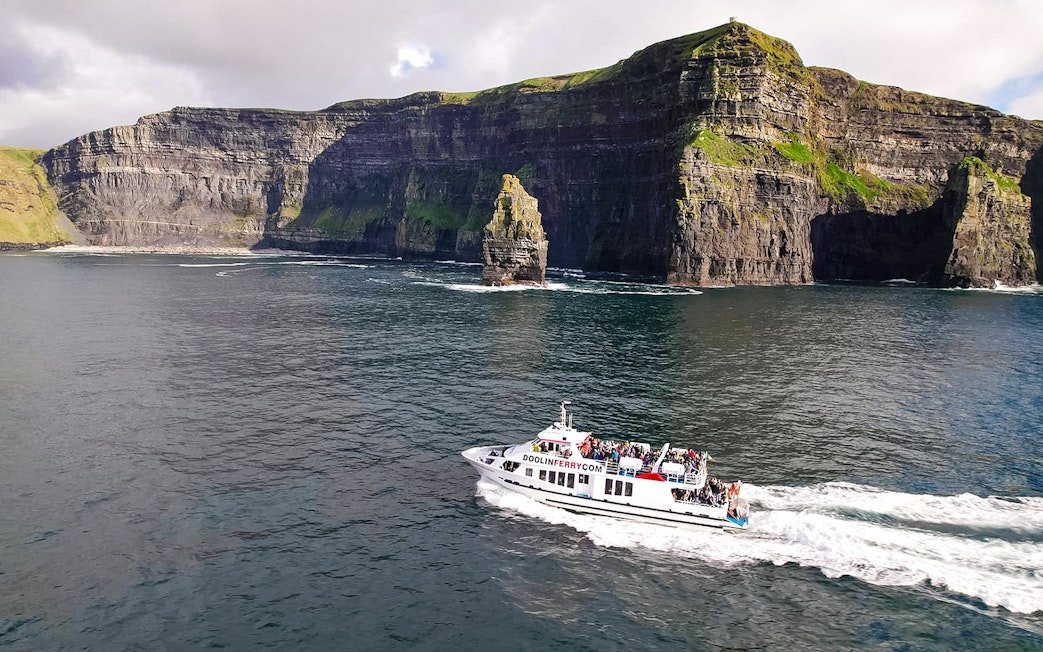 Cruise boat near Cliffs of Moher, Ireland, with passengers enjoying the view.