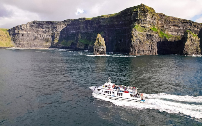 Cruise boat near Cliffs of Moher, Ireland, with passengers enjoying the view.