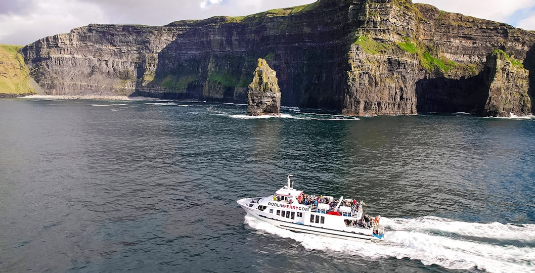 Cruise boat near Cliffs of Moher, Ireland, with passengers enjoying the view.