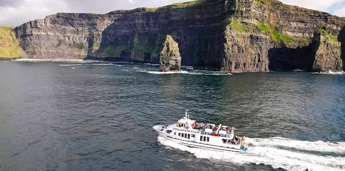 Cruise boat near Cliffs of Moher, Ireland, with passengers enjoying the view.