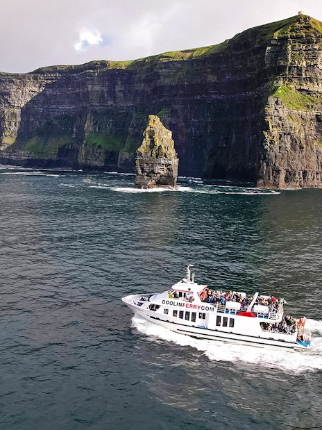 Cruise boat near Cliffs of Moher, Ireland, with passengers enjoying the view.