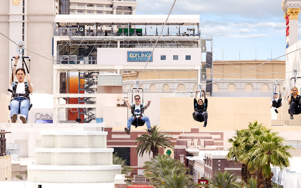 People ziplining on Fly LINQ Zipline with Las Vegas skyline in the background.