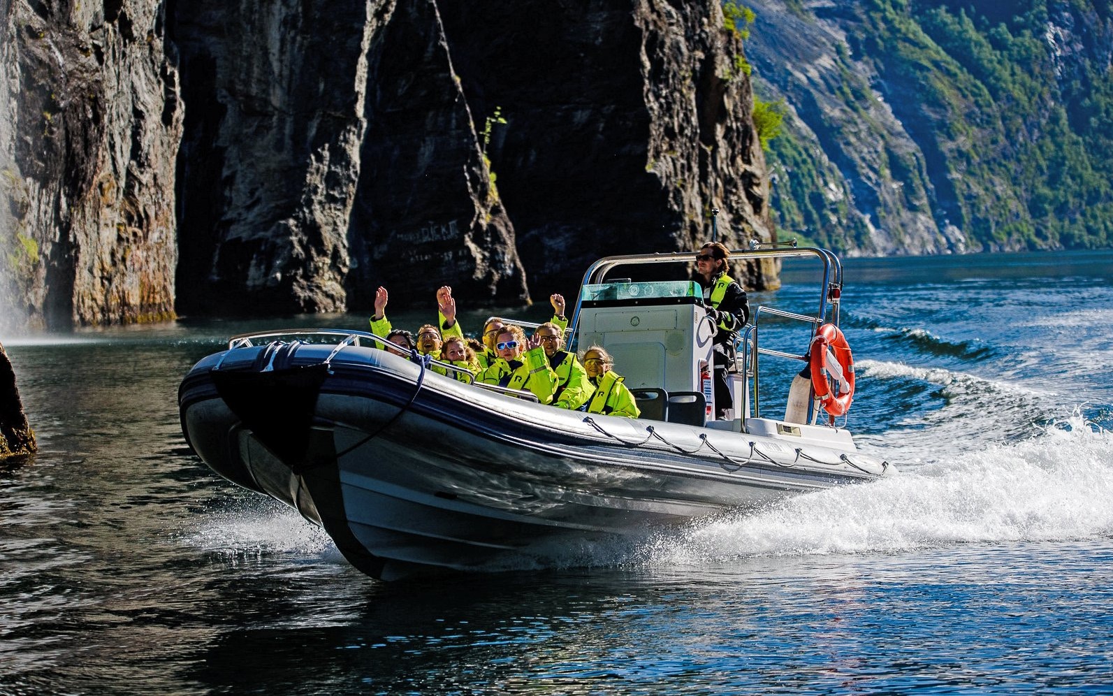 RIB boat with tourists exploring Geiranger Fjord cliffs and waterfall.