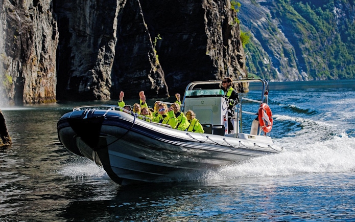 RIB boat with tourists exploring Geiranger Fjord cliffs and waterfall.