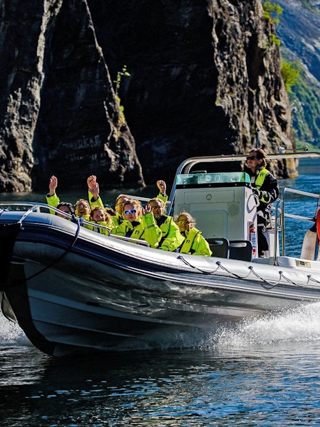 RIB boat with tourists exploring Geiranger Fjord cliffs and waterfall.
