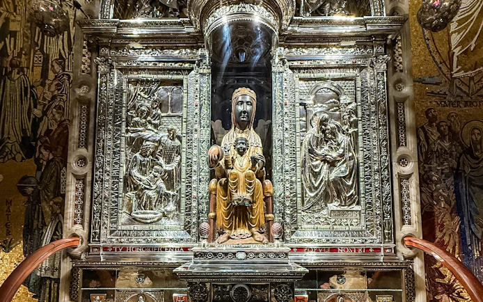 Black Madonna statue at Montserrat Monastery, Spain, surrounded by ornate carvings.