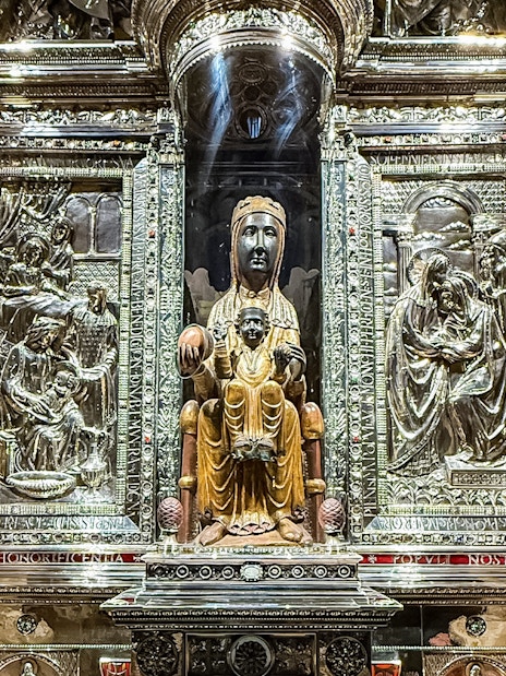 Black Madonna statue at Montserrat Monastery, Spain, surrounded by ornate carvings.