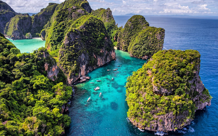 Aerial view of Phi Phi Islands' lush cliffs and turquoise waters with speedboats, Thailand.