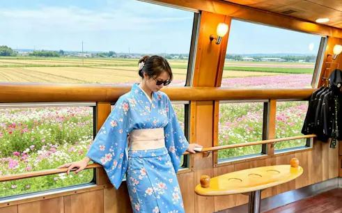 Passenger in kimono on Yufuin no Mori train with flower fields view, Fukuoka day trip.