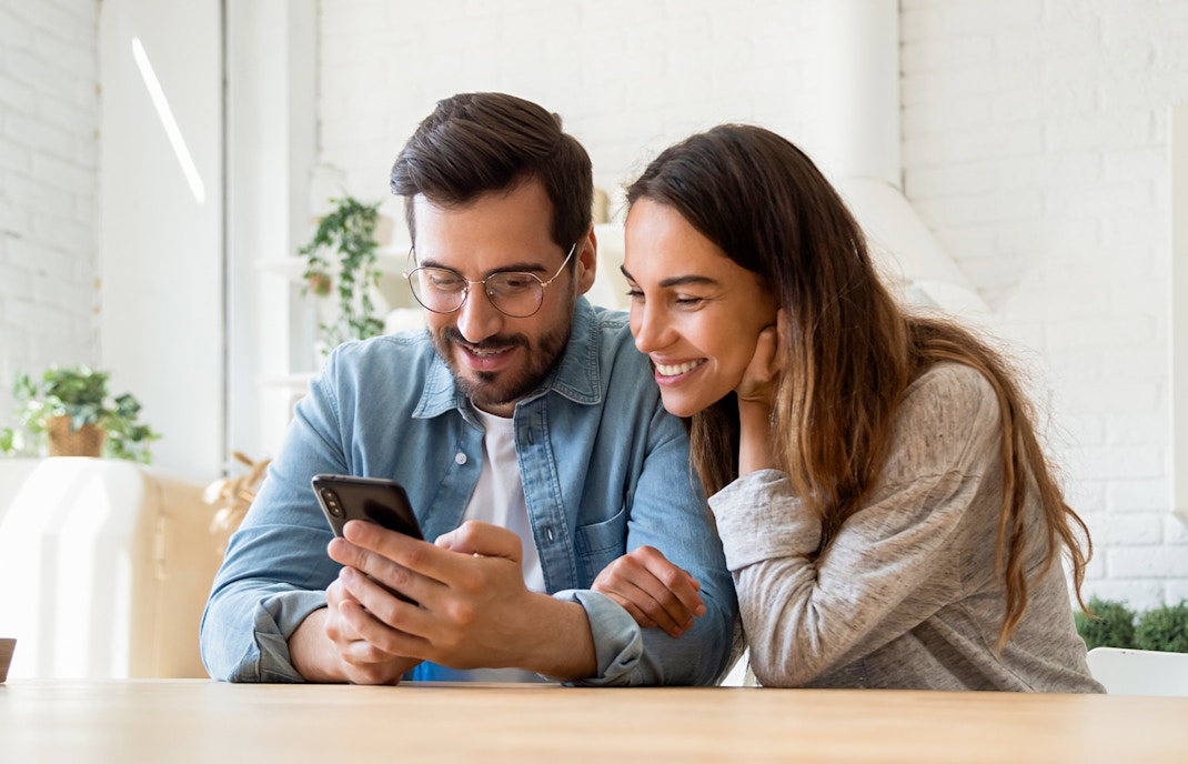 Couple joyfully discovering Online Uffizi Exhibitions on a mobile phone, sharing a moment of cultural connection in a bright modern space
