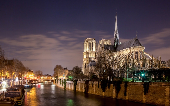 Notre-Dame Cathedral illuminated at night along the Seine River, Paris.