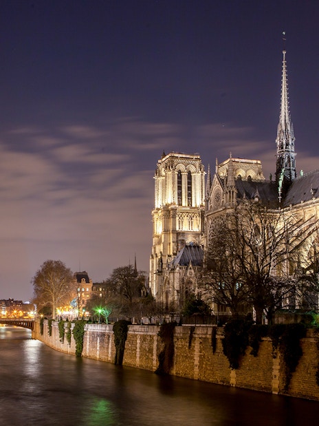 Notre-Dame Cathedral illuminated at night along the Seine River, Paris.