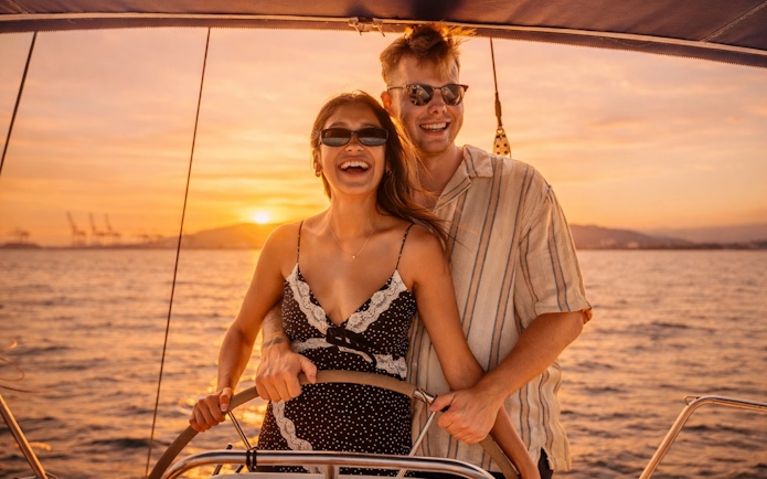 Couple steering yacht at sunset in Barcelona.