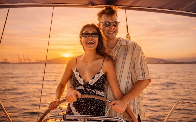 Couple steering yacht at sunset in Barcelona.
