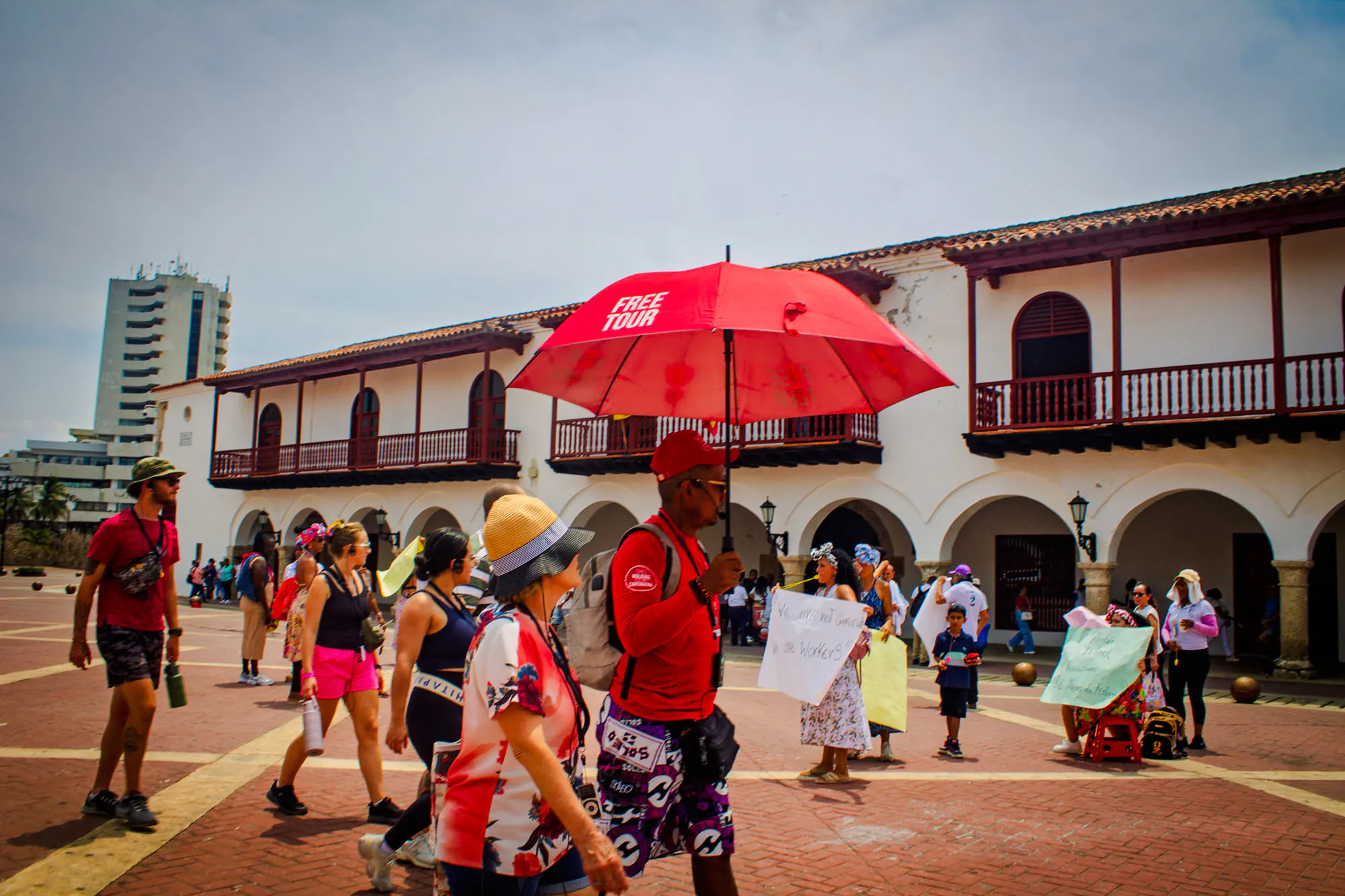 Tour group exploring Cartagena's Walled Old City with guide holding red umbrella.