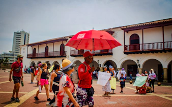 Tour group exploring Cartagena's Walled Old City with guide holding red umbrella.