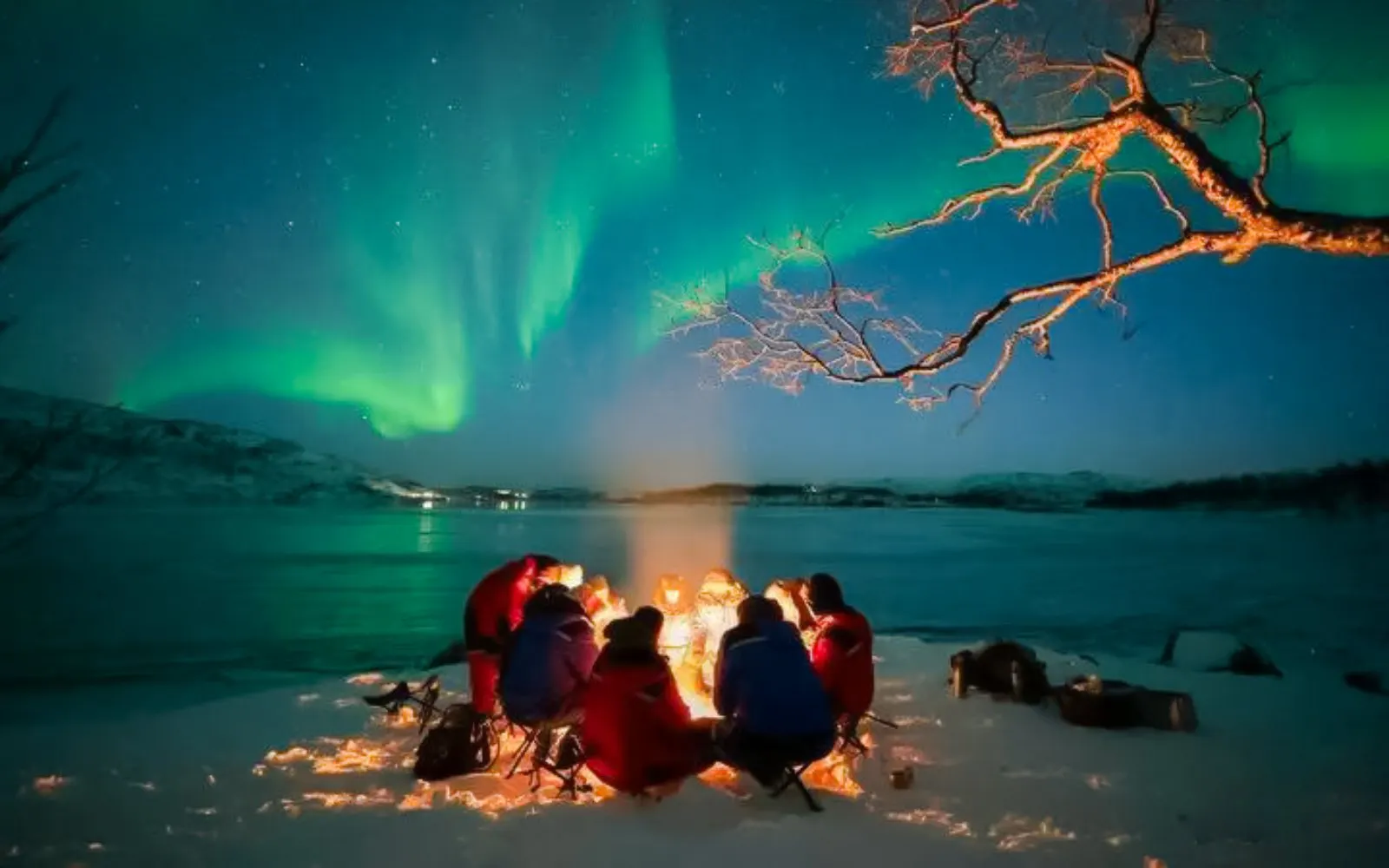 Guests gathered around a campfire under northern lights near Tromso.