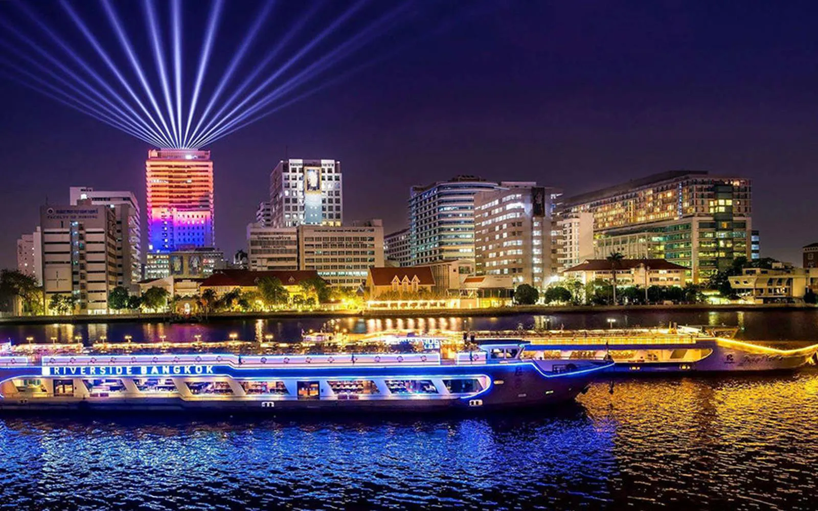 Riverside Carnival Cruise on Chao Phraya River with Bangkok skyline at night.