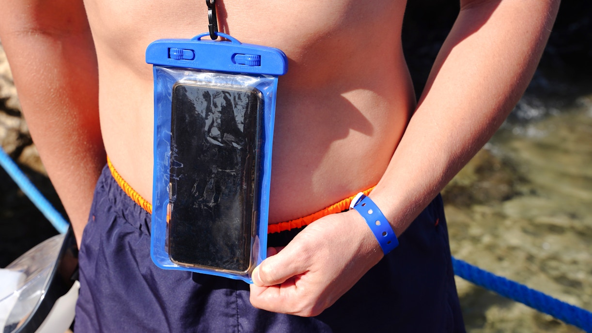 Blue waterproof smartphone case worn around neck near water.