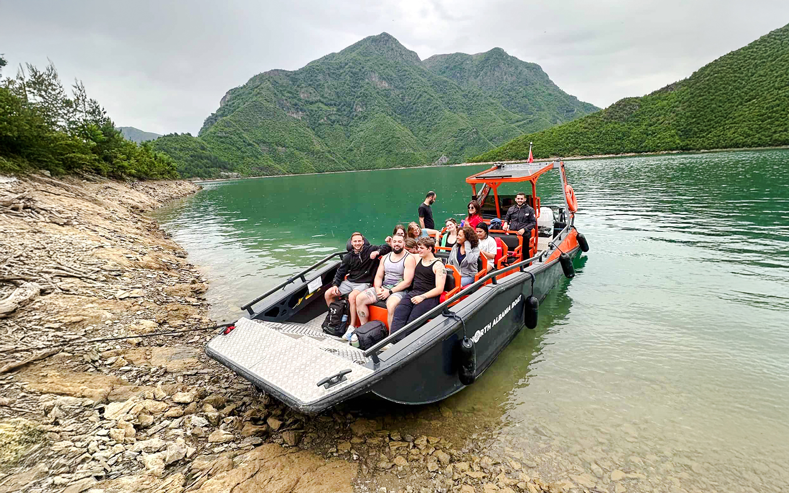 Boat with tourists on Komani Lake during Shala River tour, surrounded by green mountains.