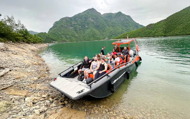 Boat with tourists on Komani Lake during Shala River tour, surrounded by green mountains.