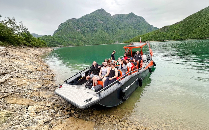 Boat with tourists on Komani Lake during Shala River tour, surrounded by green mountains.
