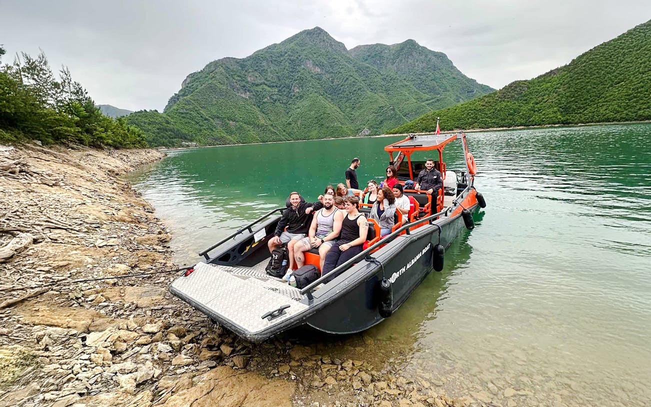 Boat with tourists on Komani Lake during Shala River tour, surrounded by green mountains.