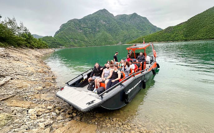 Boat with tourists on Komani Lake during Shala River tour, surrounded by green mountains.
