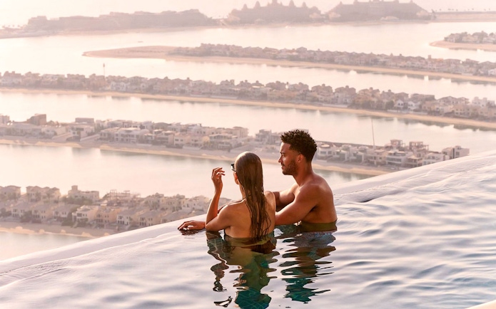 Couple enjoying the view from AURA Sky Pool overlooking Palm Jumeirah, Dubai.