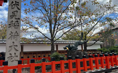 Fushimi Inari Shrine fox statue with red fence and stone pillar, Kyoto.
