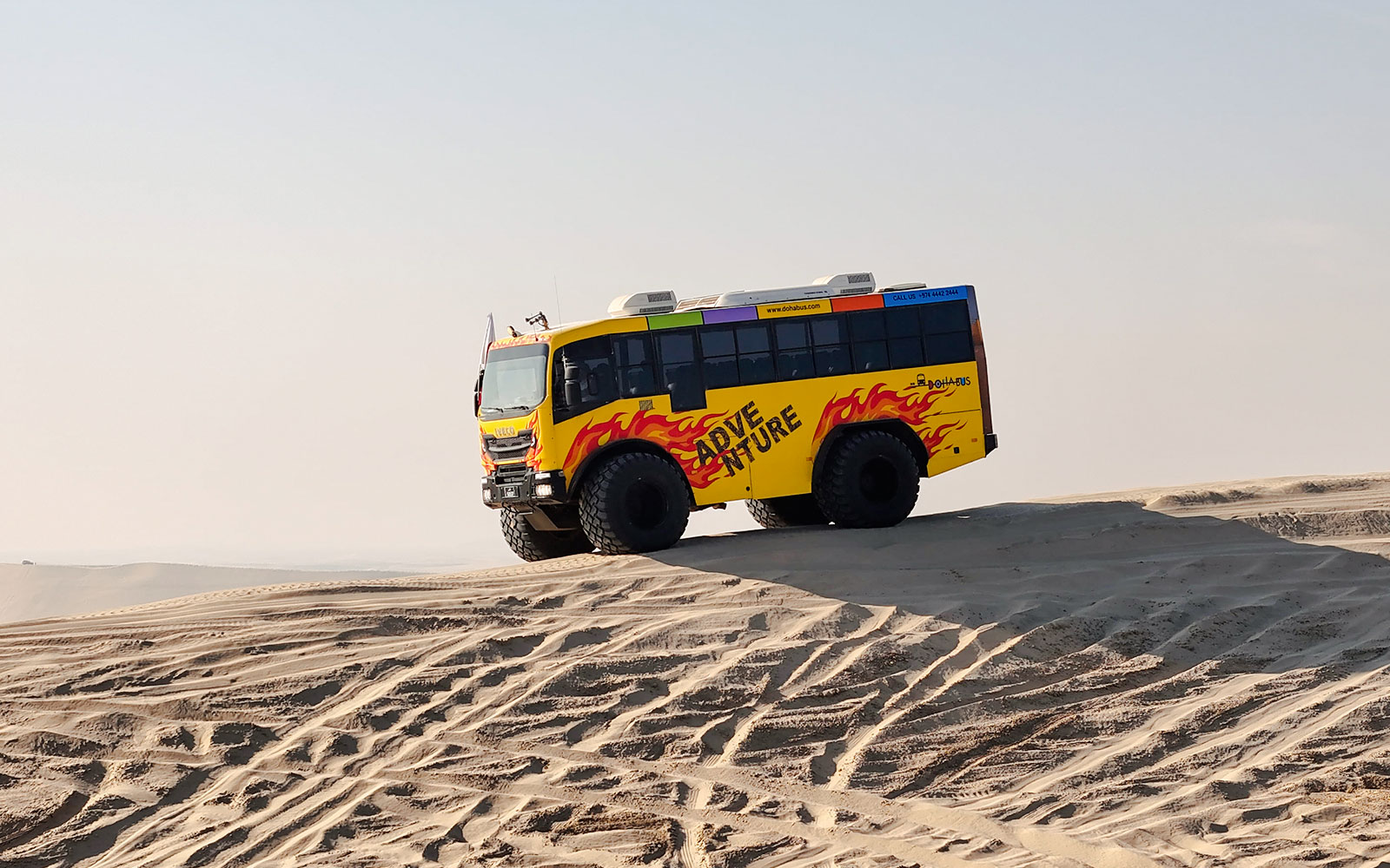 Monster bus driving over sand dunes in Doha desert.
