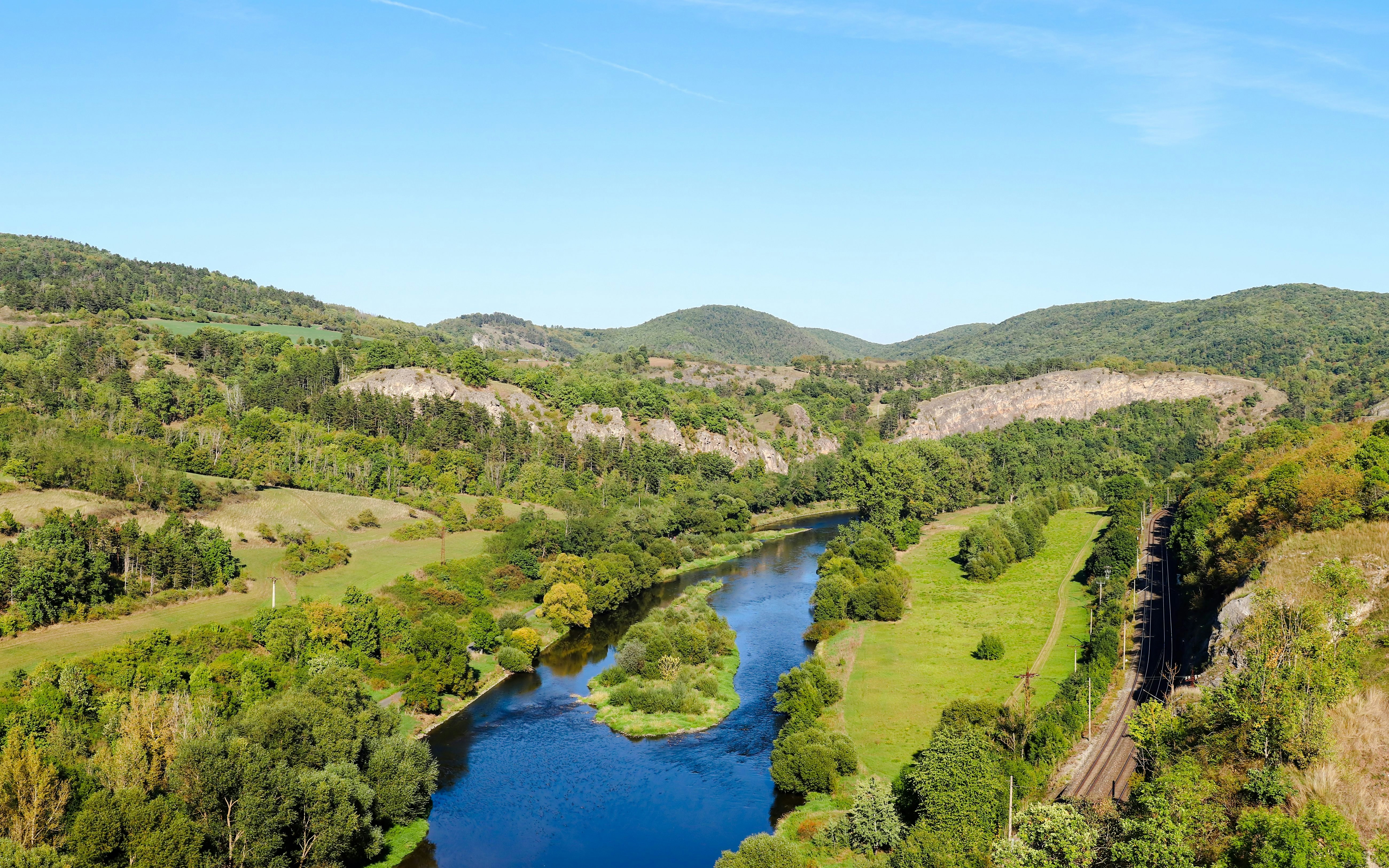 River winding through lush green landscape in Bohemian Karst, Czechia, with hills in the background.