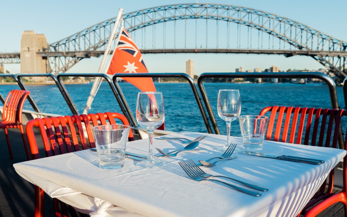 Table set for lunch on a catamaran with Sydney Harbour Bridge in the background.