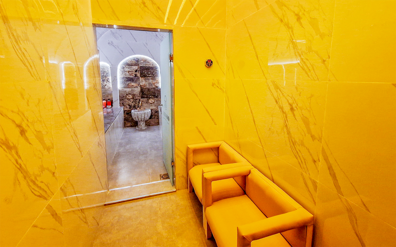 Hammam entrance with marble walls and seating area, leading to traditional spa treatment room.