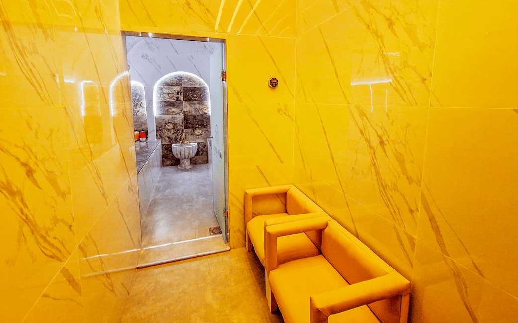 Hammam entrance with marble walls and seating area, leading to traditional spa treatment room.
