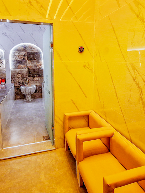 Hammam entrance with marble walls and seating area, leading to traditional spa treatment room.