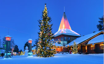Santa Claus Village with lit Christmas tree and snow-covered buildings in Rovaniemi, Finland.