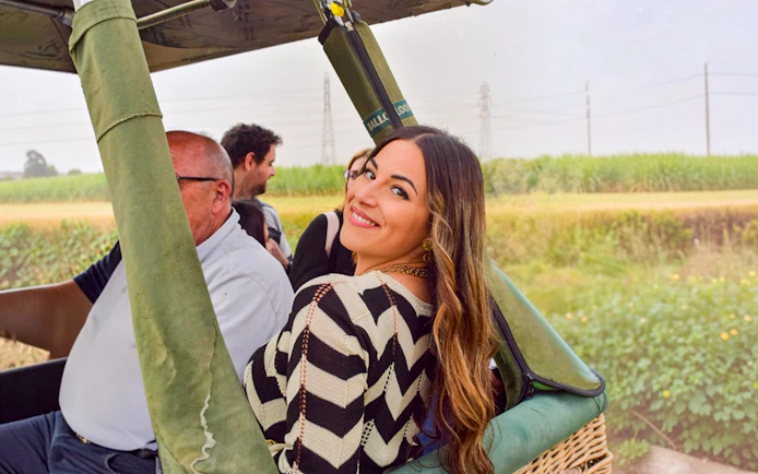 Passengers preparing for a hot air balloon ride in Luxor, Egypt, with green fields in the background.