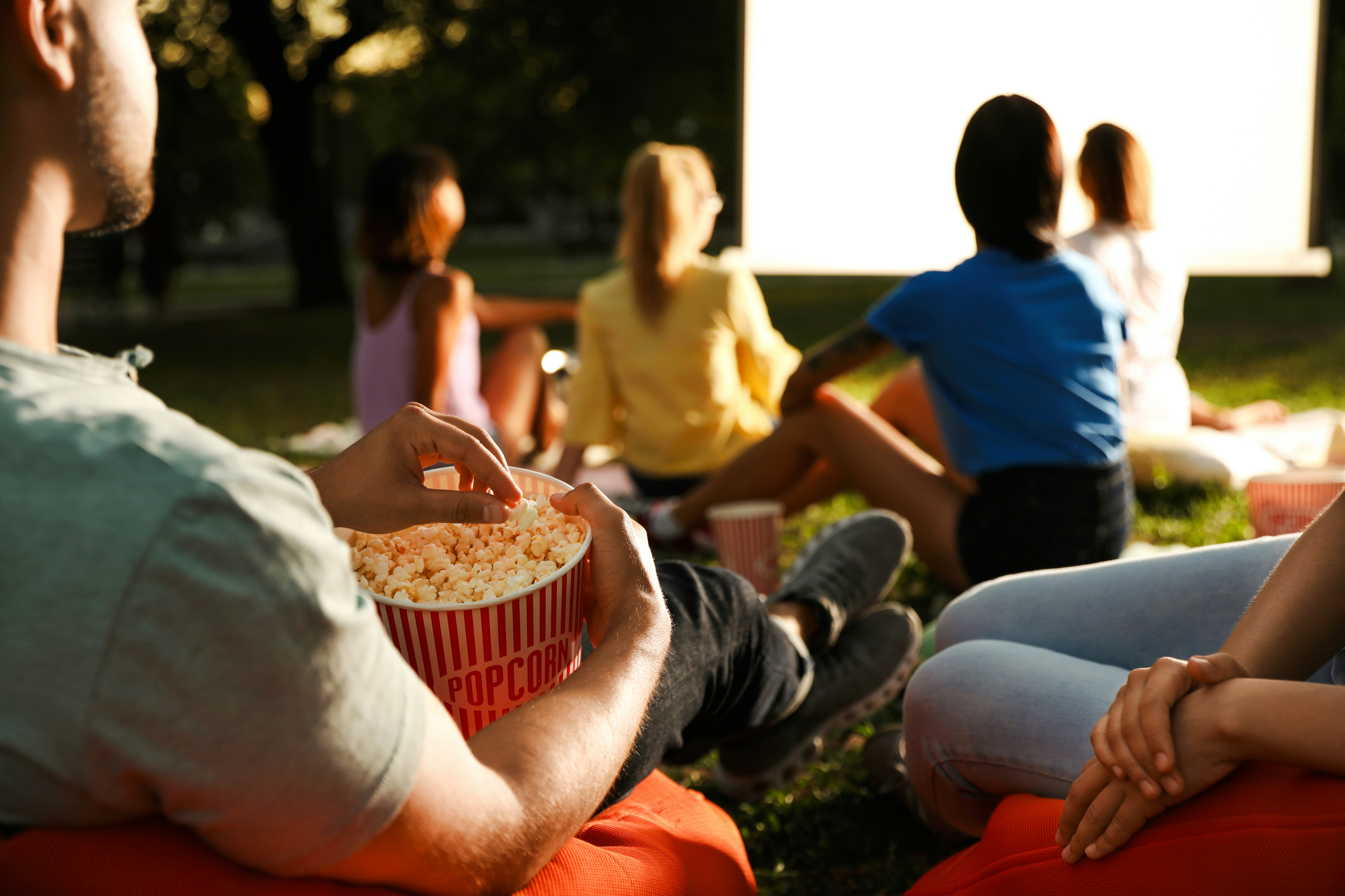 Young people enjoying popcorn while watching a movie at an outdoor cinema.