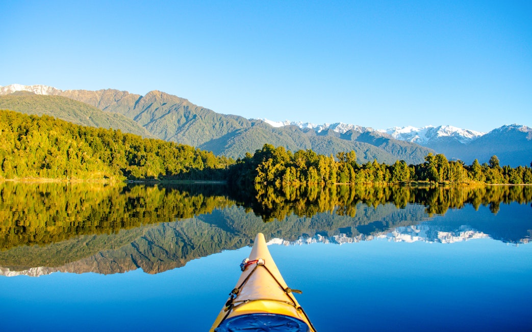 Kayak on Lake Mapourika with reflections of lush forests and mountains.