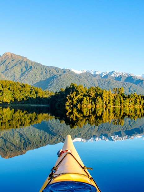Kayak on Lake Mapourika with reflections of lush forests and mountains.