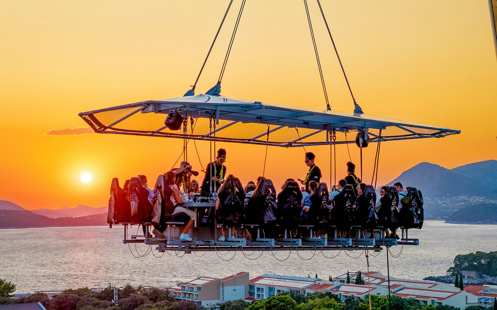 Guests dining in the sky above Dubrovnik at sunset with sea and mountains in the background.
