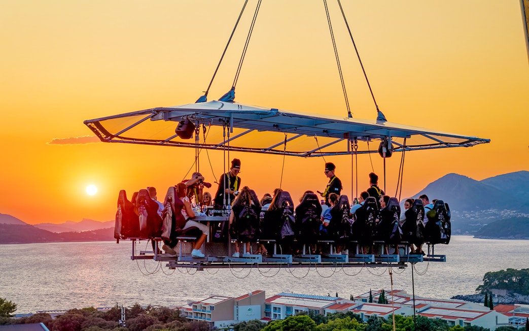 Guests dining in the sky above Dubrovnik at sunset with sea and mountains in the background.