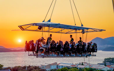 Guests dining in the sky above Dubrovnik at sunset with sea and mountains in the background.
