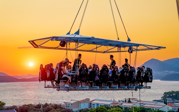 Guests dining in the sky above Dubrovnik at sunset with sea and mountains in the background.