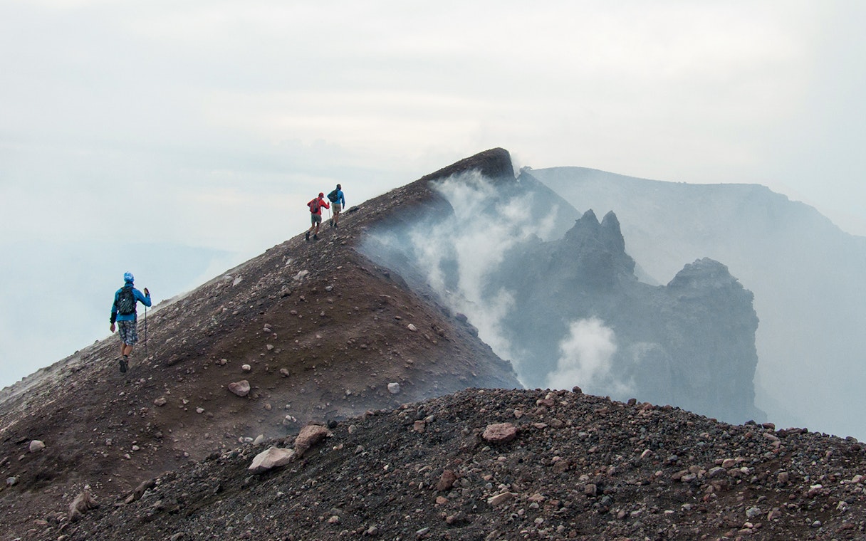 Hikers ascending Mount Etna summit crater with volcanic smoke.