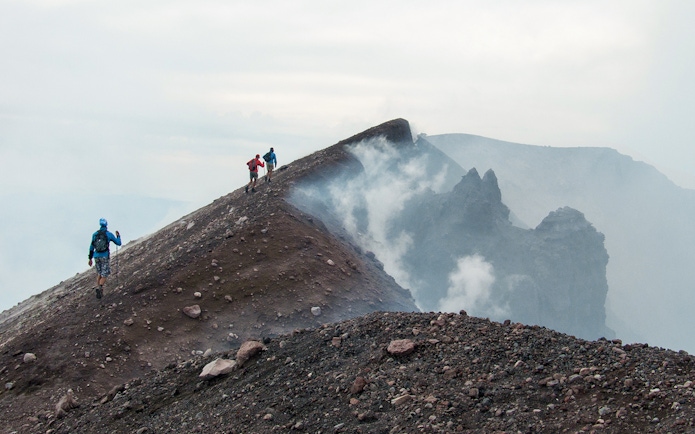 Hikers ascending Mount Etna summit crater with volcanic smoke.