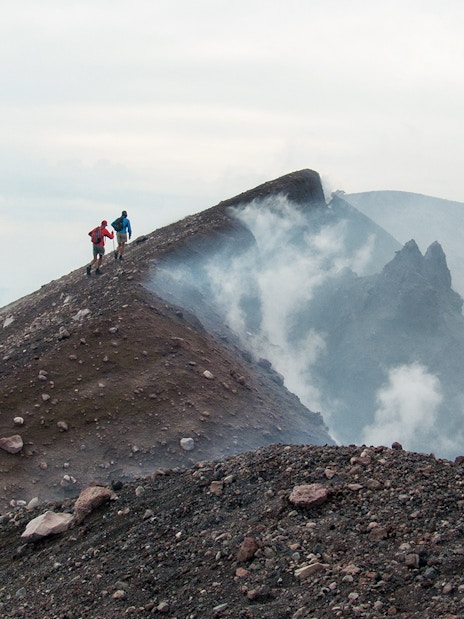Hikers ascending Mount Etna summit crater with volcanic smoke.