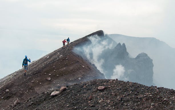 Hikers ascending Mount Etna summit crater with volcanic smoke.
